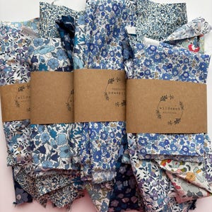 May include: Several bundles of floral fabric in shades of blue, white, and purple are displayed. Each bundle is wrapped with a brown paper band featuring the text "wildseed stitches". The fabric patterns include small flowers and leaves.
