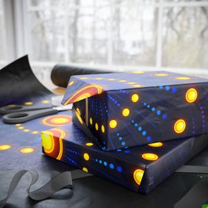 May include: Two gift boxes wrapped in dark blue paper with a pattern of yellow and orange circles and blue dots. A roll of matching wrapping paper, scissors, and a gray ribbon are also visible.