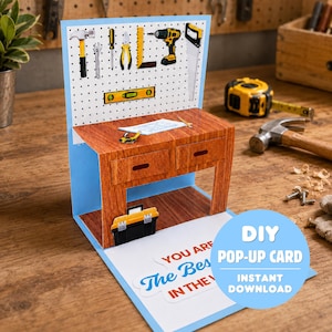 Może przedstawiać: Karta pop-up DIY z motywem warsztatu. Karta przedstawia miniaturowy warsztat z narzędziami, skrzynką narzędziową i tekstem "You Are The Best In The". Karta jest niebieska, brązowa, żółta i biała.