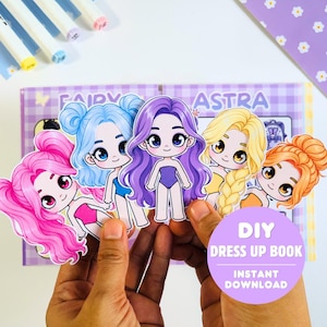 Könnte beinhalten: Ein Set aus fünf illustrierten Papierpuppen mit verschiedenen Haarfarben wie Pink, Blau, Lila, Blond und Orange, die jeweils einen Trikot tragen. Die Puppen sind vor einem lila karierten Hintergrund mit dem Text DIY DRESS UP BOOK abgebildet.
