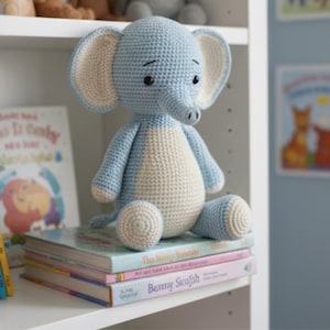 Peut inclure: Un éléphant en crochet bleu clair et crème, avec de grandes oreilles et une trompe, assis sur une pile de livres. Le jouet fait main a une expression amicale et est fabriqué en fil doux, idéal pour une chambre d'enfant.