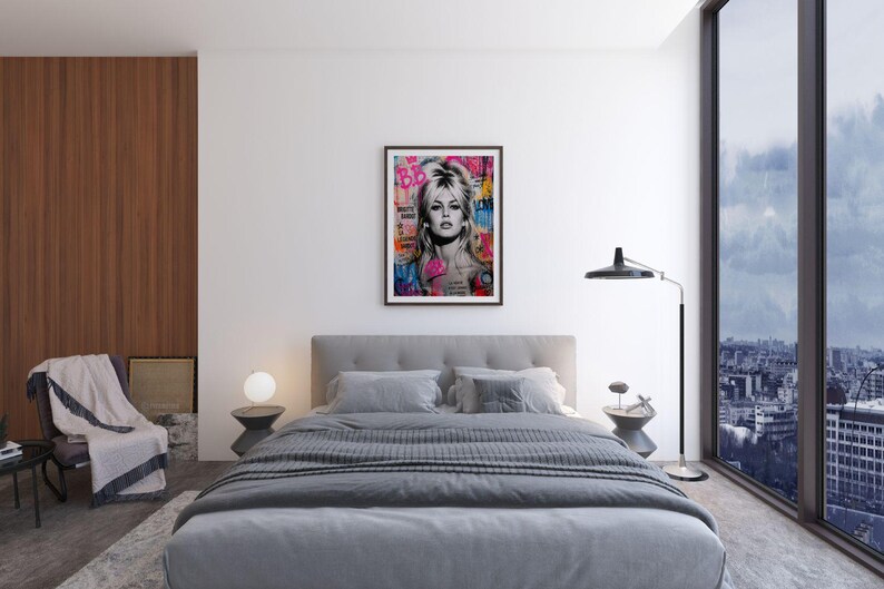 Puede incluir: Un cuadro enmarcado de arte pop con un retrato de una mujer rubia con las letras "BB" en la esquina superior izquierda. La obra de arte se exhibe sobre una cama gris con almohadas a juego y una manta gris oscura. La habitaci&oacute;n tiene un dise&ntilde;o moderno.
