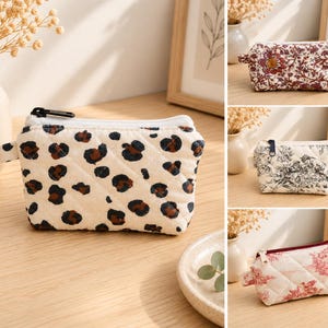 Peut inclure: Une collection de quatre petites pochettes matelassées à fermeture éclair. La pochette principale présente un fond crème avec un imprimé léopard noir et marron. Les autres modèles incluent un motif floral et deux imprimés toile en noir et rouge.