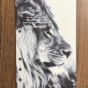 May include: Black and white print featuring a lion's profile with the text "The heart of a lion beats with unmatched strength, driven by an unquenchable desire to conquer." The print has three holes for binding.