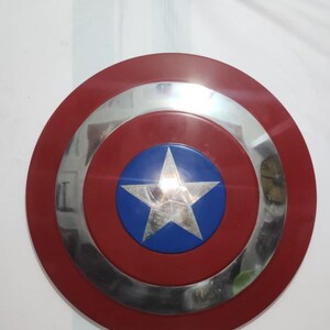 May include: A red, white, and blue shield with a silver star in the center. The shield has a circular design with a red outer ring, a silver middle ring, and a blue center with a silver star.