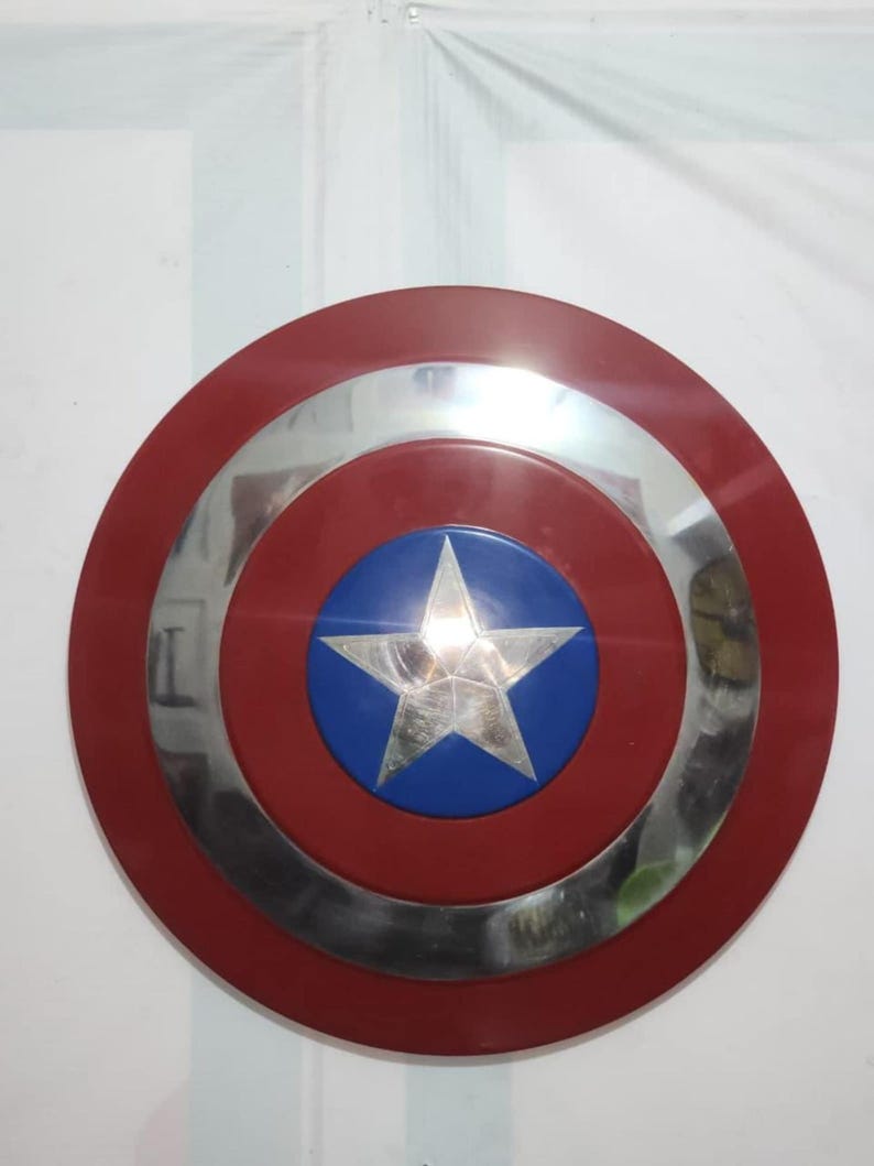 May include: A red, white, and blue shield with a silver star in the center. The shield has a circular design with a red outer ring, a silver middle ring, and a blue center with a silver star.