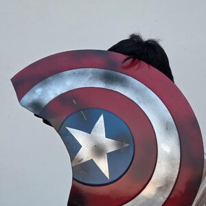 May include: A Captain America shield prop, featuring a red, white, and blue color scheme. The shield has a central blue circle with a white star, surrounded by concentric rings of silver, white, and red. The shield has a distressed, battle-worn appearance.
