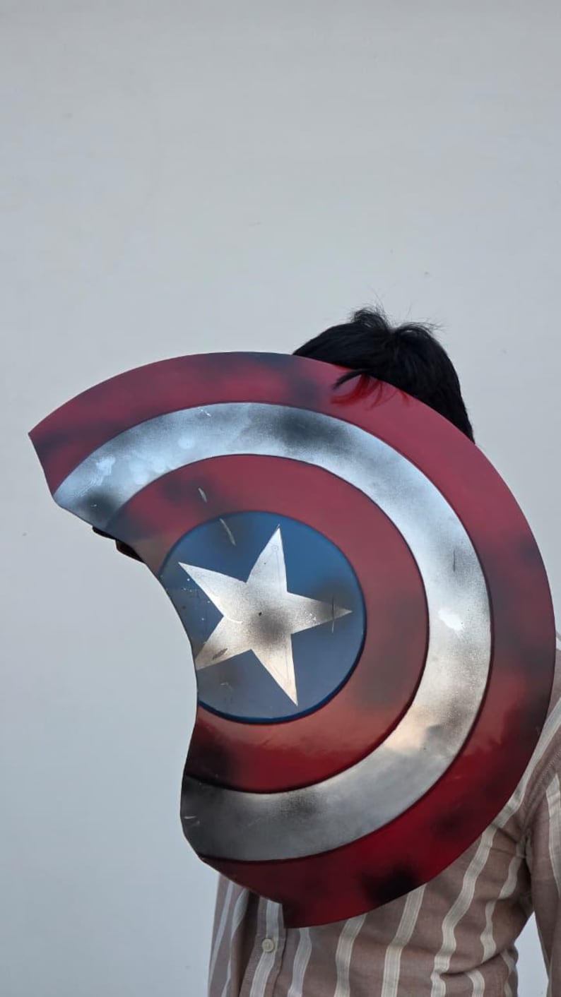 May include: A Captain America shield prop, featuring a red, white, and blue color scheme. The shield has a central blue circle with a white star, surrounded by concentric rings of silver, white, and red. The shield has a distressed, battle-worn appearance.