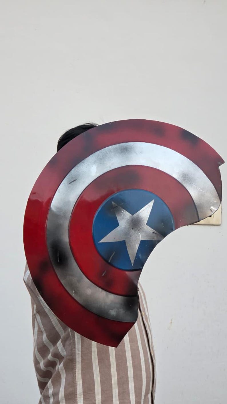 May include: A Captain America shield prop, featuring a red, white, and blue color scheme. The shield has a circular design with a white star on a blue center, surrounded by concentric red and silver rings. The prop is slightly damaged.