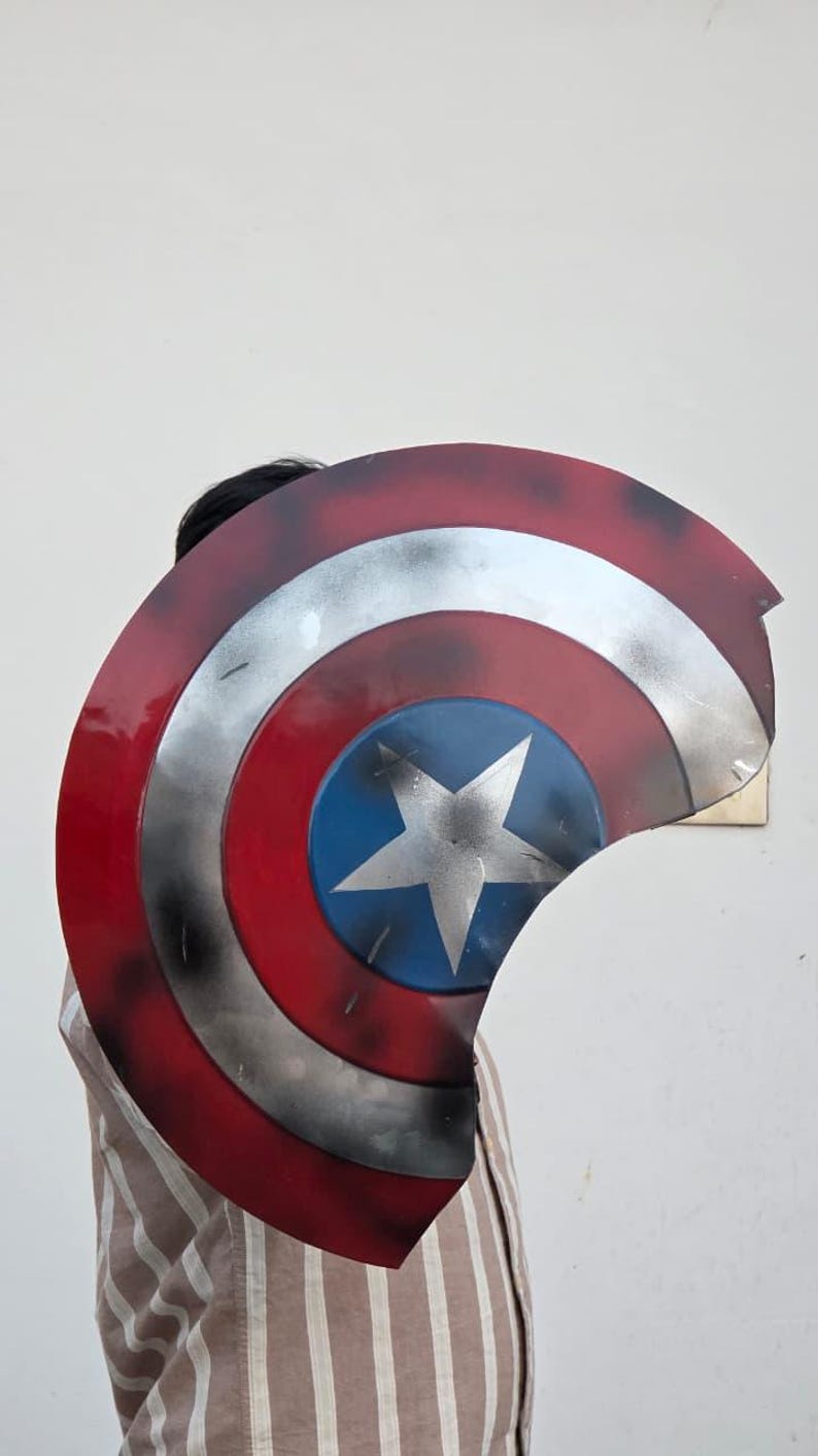 May include: A Captain America shield prop, featuring a red, white, and blue color scheme. The shield has a central blue circle with a white star, surrounded by concentric red and silver bands. The shield is slightly weathered.