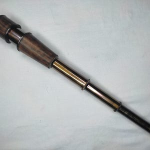 Peut inclure: Télescope de style vintage avec un oculaire en bois et un corps de couleur laiton. Le télescope a un design classique, avec une section en bois brun foncé et un tube métallique extensible. L'esthétique générale rappelle les instruments nautiques.
