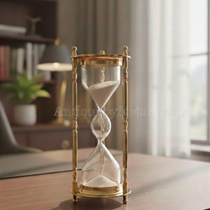 May include: An hourglass with a brass frame and clear glass bulbs. The hourglass is filled with white sand. The frame has decorative vertical bars. The hourglass is sitting on a wooden desk.