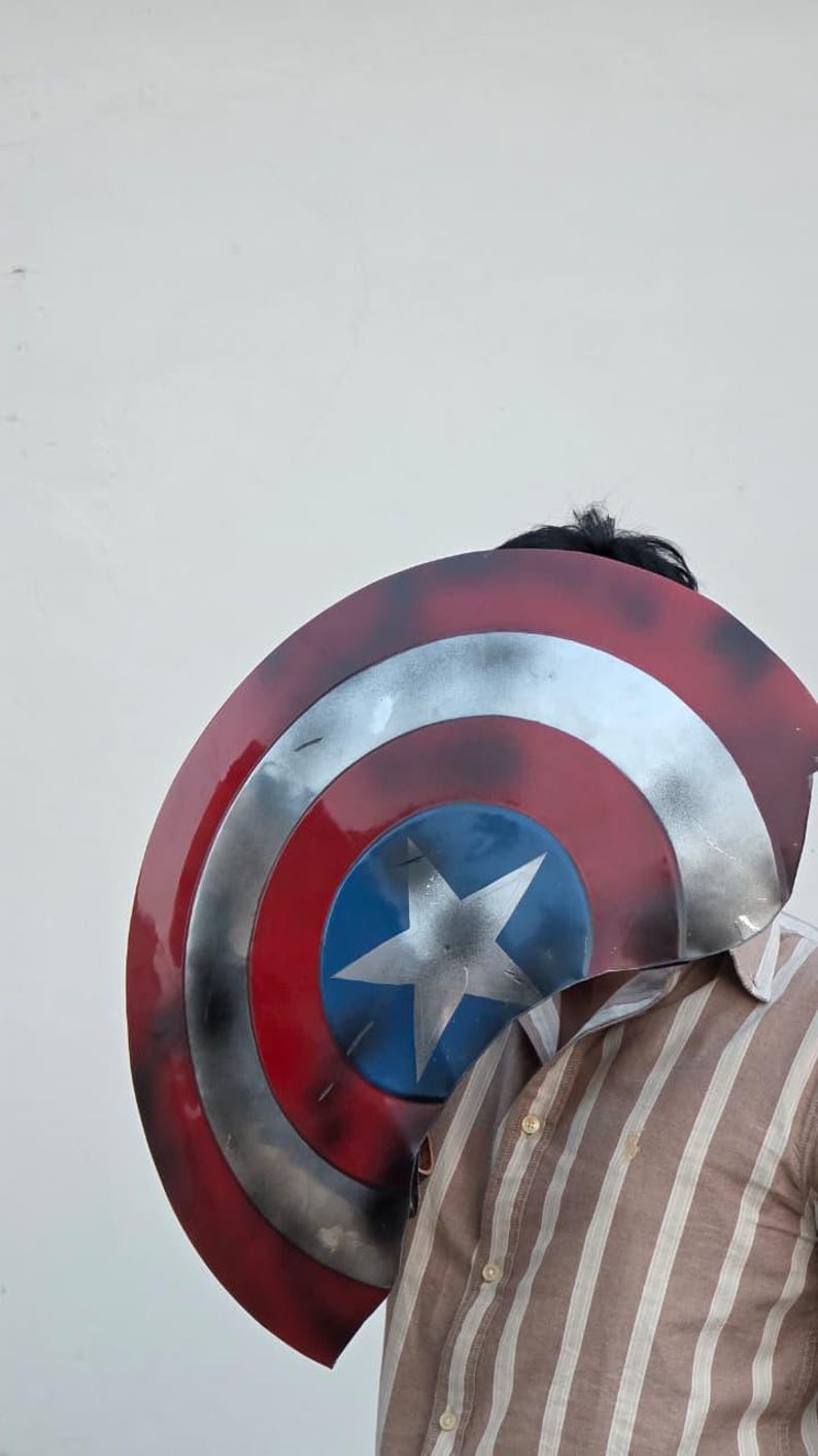 May include: A Captain America shield with a red, white, and blue color scheme. The shield features a central blue circle with a white star, surrounded by concentric rings of silver, white, and red. The shield is a prop or costume accessory.