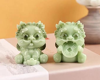 May include: Two jade-green Pixiu statues. One holds a coin in its mouth, the other a small bowl. The statues have detailed features, including wings and a textured mane. They are sitting on a pink and white surface.