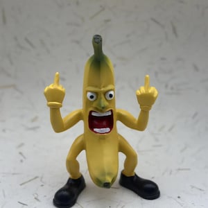 Könnte beinhalten: Eine gelbe Bananenfigur mit grünem Stiel, schwarzen Schuhen und erhobenen Armen, die mit beiden Händen den Mittelfinger zeigt. Die Banane hat einen weit geöffneten Mund und wütende Augen.