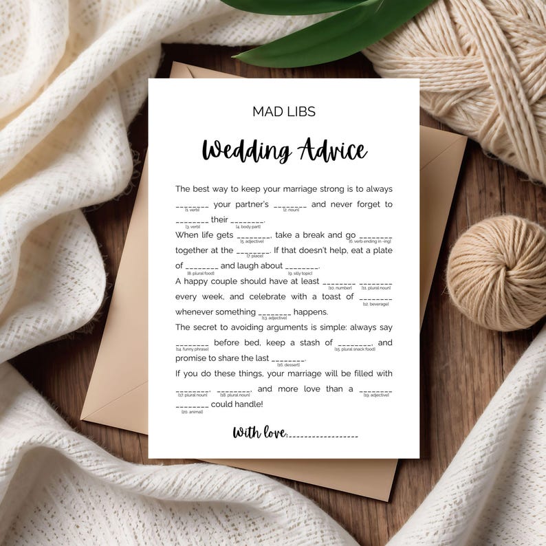May include: A white Mad Libs wedding advice card with black text, including fill-in-the-blank prompts. The card is on a wooden surface, with a beige envelope and decorative yarn in the background.