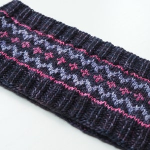 May include: A dark grey knitted headband with a pink and purple geometric pattern.