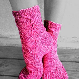 Pode incluir: Um par de meias de malha rosa com um padrão de malha de cabo. As meias são mostradas em uma superfície de madeira.