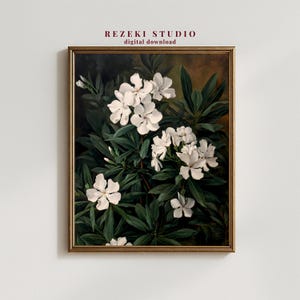 Puede incluir: Una impresión botánica enmarcada con flores blancas y hojas verdes oscuras. La obra de arte tiene una estética vintage, con el texto "REZEKI STUDIO digital download". El marco es de un marrón dorado cálido.