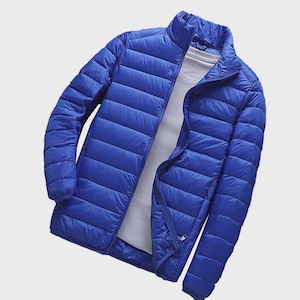 Könnte beinhalten: Eine leuchtend blaue, gesteppte Daunenjacke mit Stehkragen, langen Ärmeln und einem durchgehenden Frontreißverschluss. Die Jacke wird über einem schlichten weißen T-Shirt getragen und zeigt eine leichte, horizontal gesteppte Konstruktion.