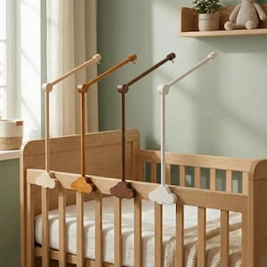 May include: Four wooden baby mobile arms in varying shades of brown and white are attached to a light-colored wooden crib. Each arm has a cloud-shaped base and a curved top with a hook for hanging toys.