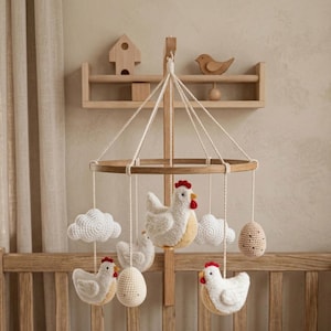 Peut inclure: Mobile pour bébé en bois avec un cadre circulaire, orné de poulets, d'œufs et de nuages en crochet suspendus. Les poulets ont des crêtes rouges et des ventres jaunes. Le mobile est suspendu au-dessus d'un lit bébé en bois.