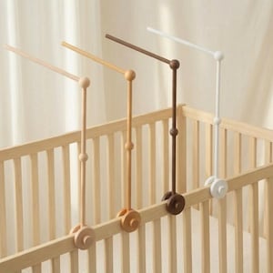 May include: Four wooden baby mobile arms in natural, light brown, dark brown, and white. Each arm is attached to a wooden wheel and has a ball-shaped accent. The mobiles are mounted on a light-colored wooden crib.
