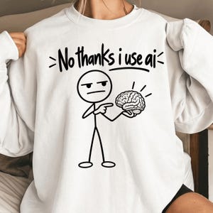 May include: A white long-sleeve sweatshirt featuring a black graphic of a stick figure pointing at a brain. Above the figure, the text reads, "No thanks i use ai" in a bold, handwritten-style font. The design is centered on the chest area.