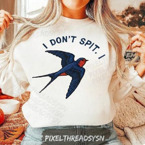 May include: White sweatshirt with the text "I DON'T SPIT. I" above a blue and red swallow bird graphic. The sweatshirt is a long-sleeved, casual top.
