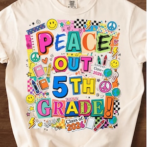 Puede incluir: Camiseta color crema con un gráfico colorido que dice "PEACE OUT 5TH GRADE! Class of 2026." El diseño incluye caras sonrientes, estrellas, corazones, símbolos de paz y elementos escolares.