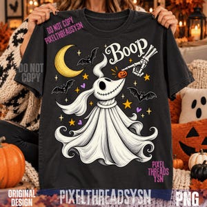 Puede incluir: Una camiseta negra con un gráfico de un perro fantasma blanco con orejas largas, boca cosida y cuerpo fluido. Una mano esquelética toca la nariz del perro, que tiene una pequeña calabaza. El diseño incluye una luna creciente amarilla, murciélagos, estrellas y la palabra Boop.