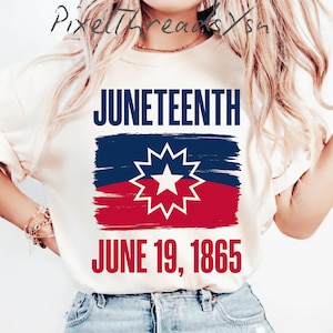 May include: A cream-colored t-shirt featuring the text JUNETEENTH in dark blue, a graphic of the Juneteenth flag with a white starburst, and the text JUNE 19, 1865 in red. The design is centered on the chest of the short-sleeved crew neck shirt.