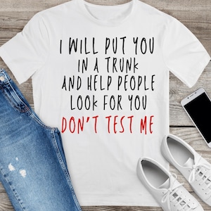 May include: White t-shirt with the text "I WILL PUT YOU IN A TRUNK AND HELP PEOPLE LOOK FOR YOU DON'T TEST ME" in black and red. The shirt is paired with blue jeans and white sneakers.