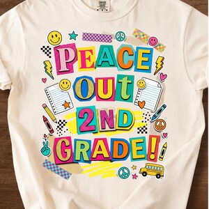 May include: Cream-colored t-shirt with a colorful graphic that reads "PEACE OUT 2ND GRADE!!" The design includes smiley faces, stars, lightning bolts, hearts, and a school bus. The text is in various bright colors.