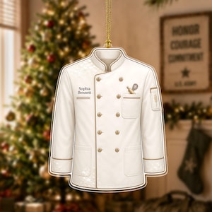 May include: A white chef coat ornament with gold trim, featuring the name Sophia Bennett printed on the chest, a small whisk and rolling pin graphic in the pocket, and a wheat stalk icon on the sleeve, suspended by a gold cord.