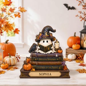 May include: A decorative figurine featuring a white ghost wearing a witch hat and reading a book, perched atop a stack of four books titled Ghostly Tales, Spells & Shadows, Potions & Poetry, and Legends of the Night, with a nameplate reading SOPHIA.