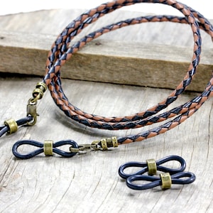 May include: A braided leather eyeglass chain with black and brown leather strands. The chain has two metal clasps and two black rubber loops with metal accents.
