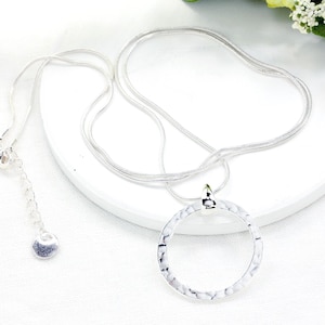 May include: A silver-toned necklace with a large, textured, open circle pendant. The necklace has a delicate chain and an adjustable clasp. The pendant is a hammered metal design, adding a unique touch to the jewelry.