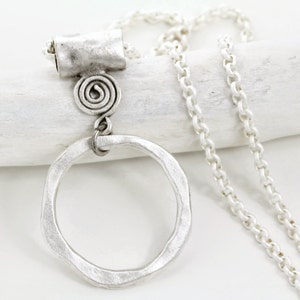 May include: A silver-toned necklace with a large, irregular circle pendant. The pendant hangs from a chain and features a textured finish. The necklace also has a spiral design element. The chain is approximately 20 inches long.