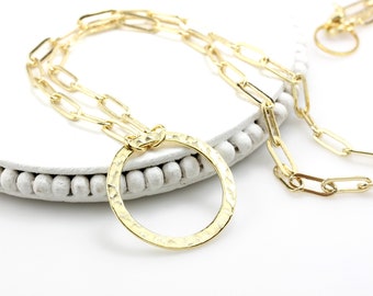 May include: A gold necklace with a large, hammered circle pendant and a chain made of linked ovals.