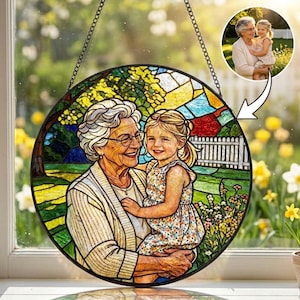 May include: A circular stained glass panel depicting a grandmother and granddaughter in a garden setting. The artwork is framed by a black border and suspended by a chain. A smaller image of the pair is in the upper right corner. The panel is a decorative item.