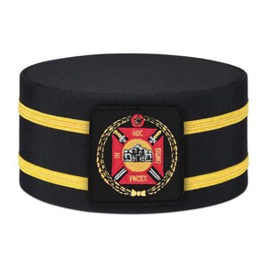 May include: A black pillbox-style hat featuring two horizontal gold bands encircling the base. Centered on the front is a square patch displaying a red cross, two crossed swords, a central building illustration, and the text In Hoc Signo Vinces.