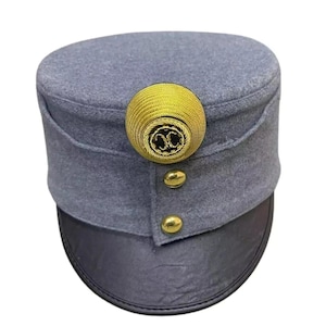 Pode incluir: Um chapéu militar cinzento com aba cinzenta escura. O chapéu apresenta um grande botão decorativo dourado e dois botões dourados menores. Provavelmente um item histórico ou vintage.