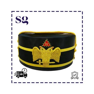 Puede incluir: Sombrero negro con bordados dorados, incluyendo un águila bicéfala y el número 32 en un triángulo rojo. El sombrero tiene ribetes dorados y forma cilíndrica, posiblemente para uso ceremonial. (aprox. 20 cm de diámetro)