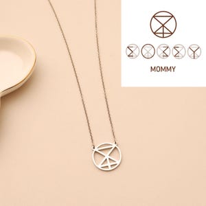 May include: A silver-colored necklace with a circular pendant featuring a geometric design. The necklace hangs on a delicate chain. The word "MOMMY" is displayed in a brown font next to a series of similar geometric shapes.