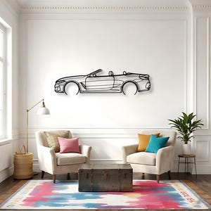 May include: A black metal wall art piece depicting the side profile of a convertible car. The artwork is mounted on a white wall above two armchairs, a trunk, and a colorful rug. The car outline is detailed, showing the wheels and interior.