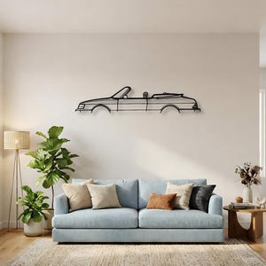 May include: A black metal wall art piece depicting the side profile silhouette of a convertible car. The linear design features the outline of the windshield, the open top, the body panels, and the wheel arches, mounted horizontally on a wall.