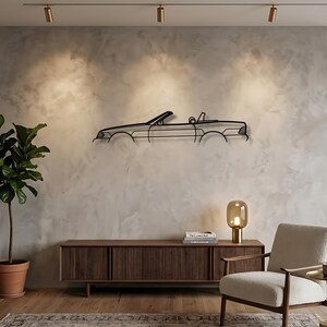 May include: A black metal wall art piece featuring the minimalist outline of a convertible car. The linear design captures the side profile of the vehicle, including the windshield, seats, and body frame, mounted horizontally on a wall.