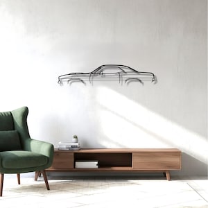 May include: A black metal wall art piece depicting the side profile of a classic muscle car. The artwork is mounted on a white wall above a wooden media console. A green armchair is in the foreground.