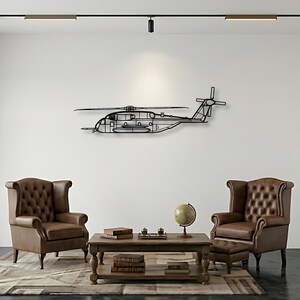 May include: A black metal helicopter wall art piece is mounted on a white wall. The artwork is a detailed outline of a helicopter, with visible rotors and tail. The room features two brown leather armchairs and a wooden coffee table.